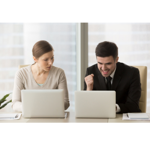 A woman enviously looks into a coworkers success on his laptop as he celebrates.